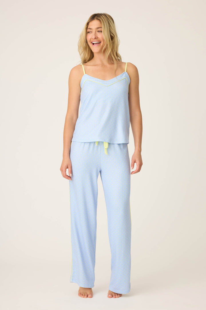 A woman stands barefoot against a plain backdrop, smiling and looking to the side, wearing the P.J. Salvage Beautiful Life Polka Dot Pants Set: light blue pajama pants and a matching camisole top with yellow trim.