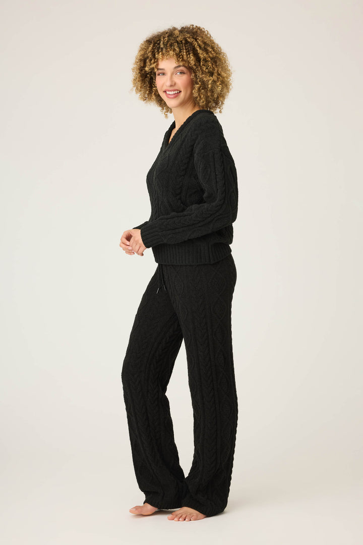 A person with curly hair stands barefoot on a light background, smiling at the camera while wearing the P.J. Salvage SOLID PJ SET COZY CHENILLE CABLE KNIT.