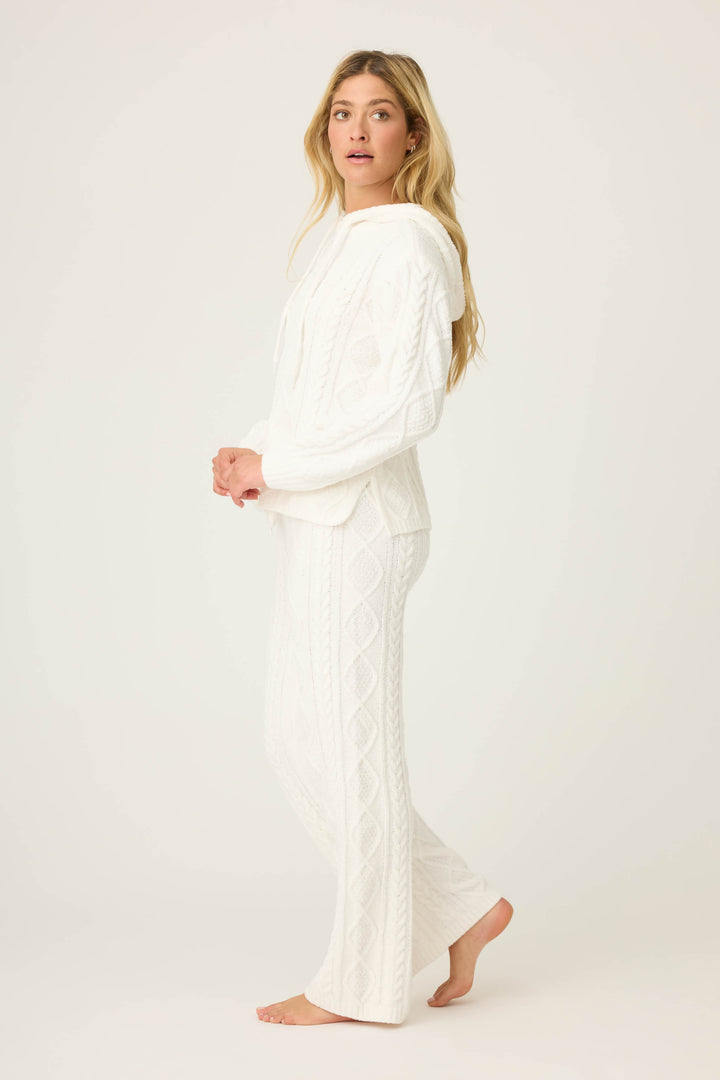 A person stands barefoot on a light background, wearing the P.J. Salvage SOLID PJ SET COZY CHENILLE CABLE KNIT in white, featuring a textured knit hooded sweater and matching pants, facing sideways with their head turned slightly toward the camera.