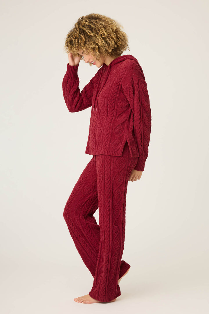 A person with curly hair stands barefoot, facing sideways and looking down, wearing the P.J. Salvage SOLID PJ SET COZY CHENILLE CABLE KNIT against a plain light background, with one hand touching their head.