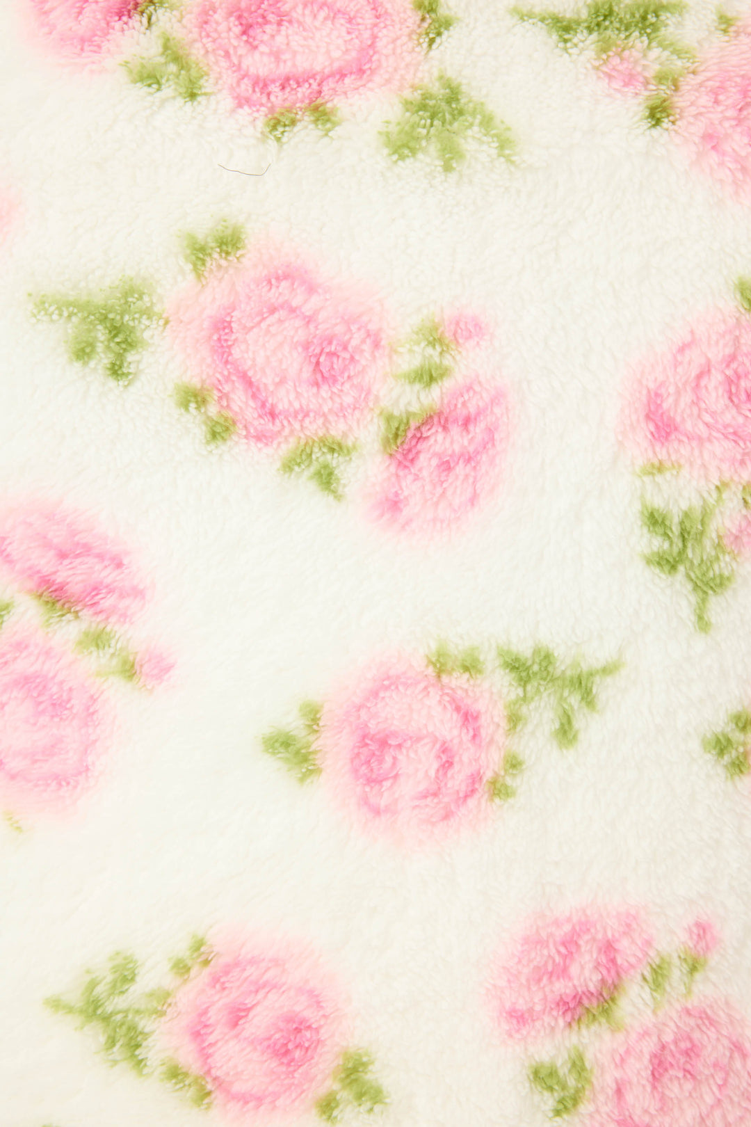 A close-up of the Lets Get Cozy Plush Floral Print Blanket by P.J. Salvage shows its soft white fabric with a cozy, fuzzy feel and a printed pattern of pink roses and green leaves.