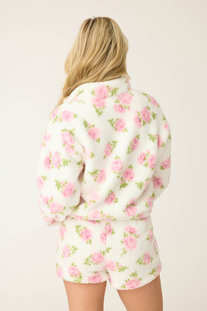 A person with long blonde hair is seen from the back wearing the P.J. Salvage Lets Get Cozy Floral Print Jacket, a fuzzy white piece featuring a pink and green floral pattern.