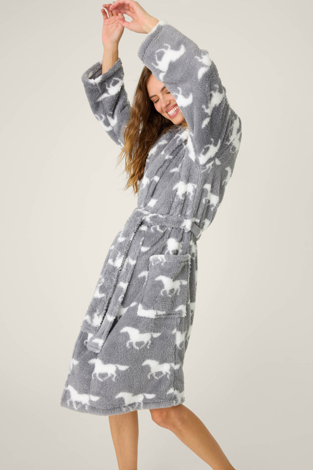 A woman smiles and raises her arms while modeling the P.J. Salvage STARS ROBE ROBE LETS GET COZY, a gray knee-length bathrobe with a white dog pattern, against a plain light background.