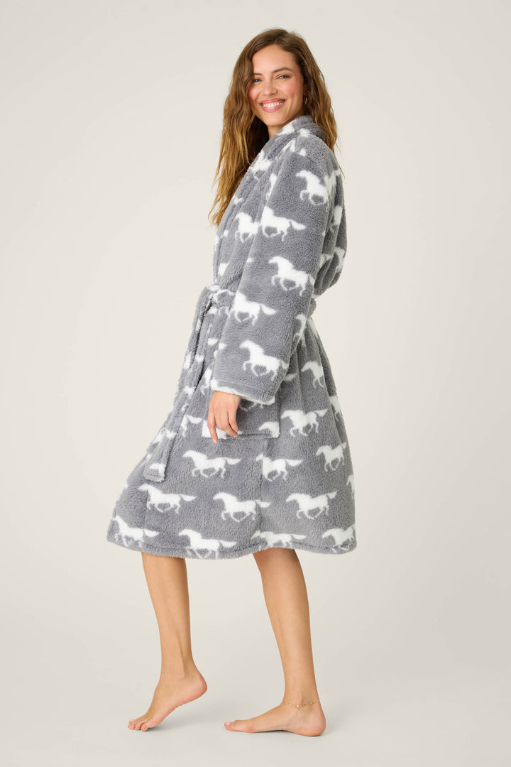 A person stands barefoot against a plain backdrop in the P.J. Salvage STARS ROBE ROBE LETS GET COZY, a grey knee-length robe with long sleeves, pockets, belt, and white dinosaur print. They smile and glance over their shoulder.