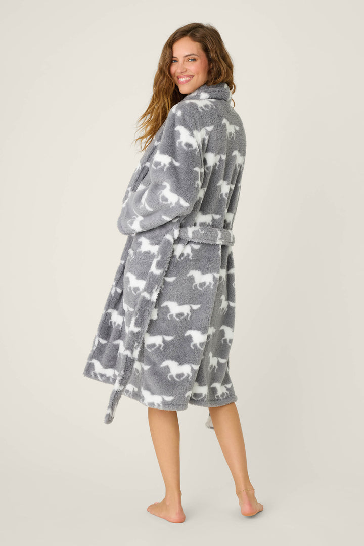 A woman stands barefoot and smiling, wearing the P.J. Salvage STARS ROBE ROBE LETS GET COZY. The cozy grey fleece robe with a belt falls below her knees and features a white horse pattern. She looks over her shoulder, slightly turned to the side.