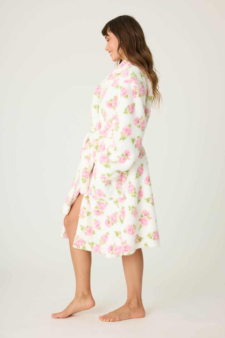 A woman stands barefoot in profile, wearing the P.J. Salvage Lets Get Cozy Floral Print Robe—knee-length, white with a pink floral pattern, and belted at the waist—against a plain light background.