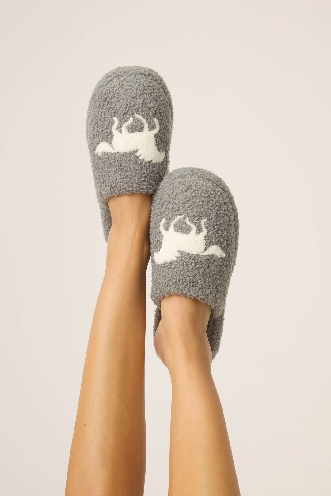 A person’s legs are raised, wearing P.J. Salvage Let's Get Cozy Horse Fleece Slippers with a horse design on top, set against a plain light background.