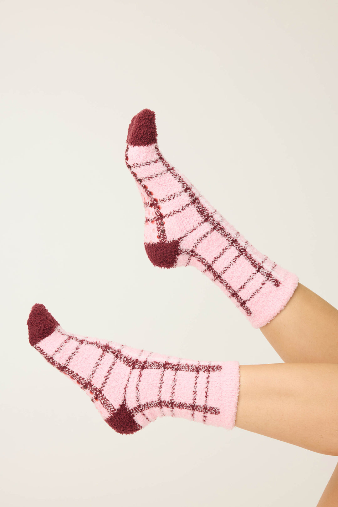 Two feet wear P.J. Salvage PLAID SOCKS LETS GET COZY—fuzzy pink socks with a brown plaid pattern and solid brown heels and toes—raised against a plain, light background.