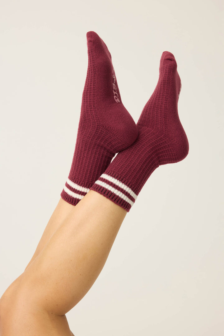 A pair of legs raised in the air wears P.J. Salvage SOLID SOCKS LETS GET COZY—maroon ribbed socks with two white stripes near the top—against a plain light-colored background.