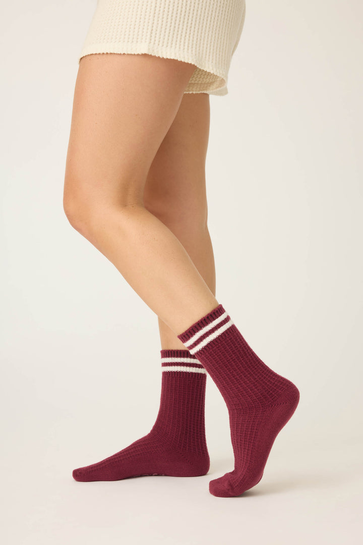 A person showcases the lower half of their body in cream shorts and P.J. Salvages SOLID SOCKS LETS GET COZY—burgundy socks with two white stripes—standing against a simple light background.