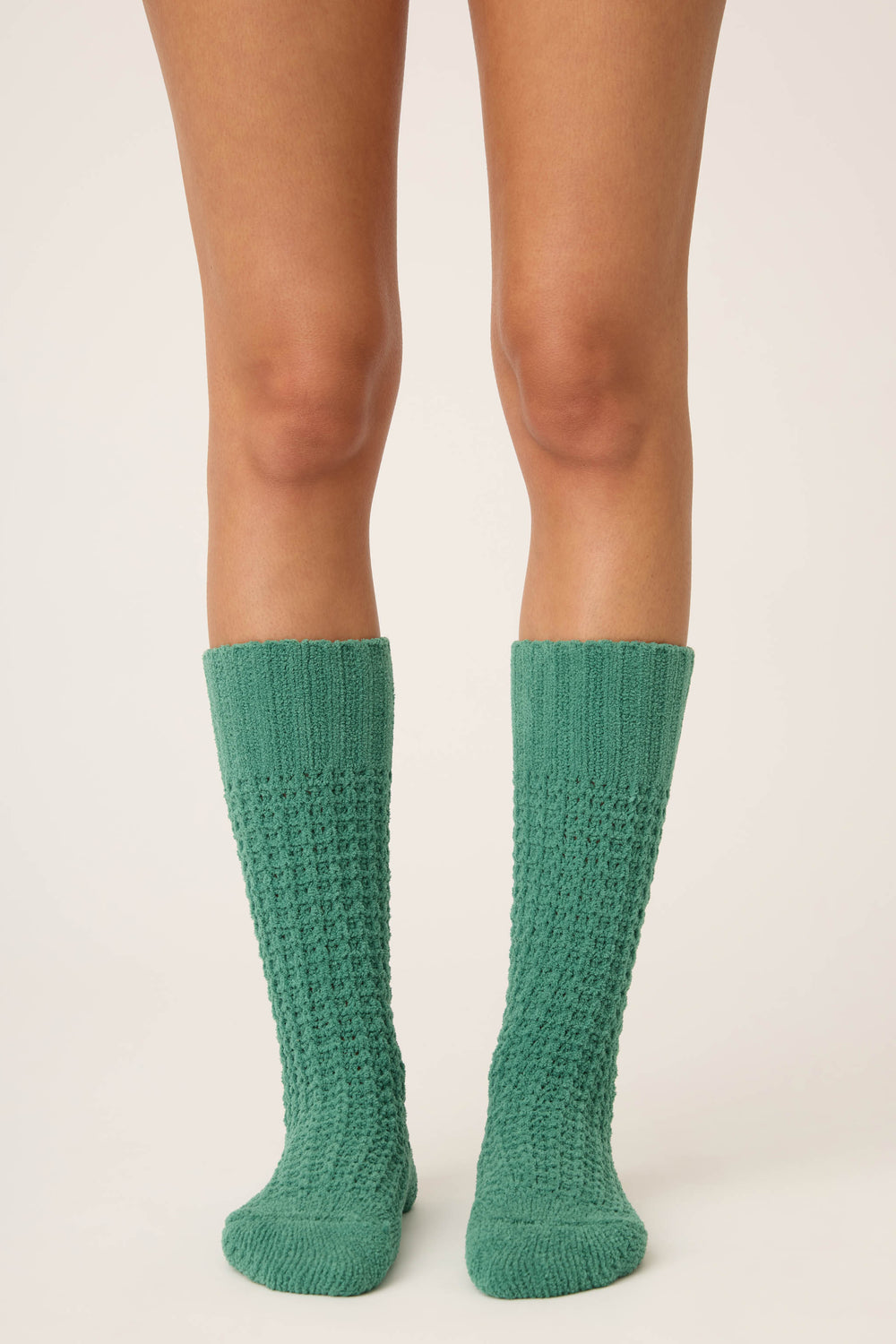 A person stands on a neutral background, wearing P.J. Salvage Chenille Waffle Solid Crew Socks in green. Only the lower legs and feet are visible, with toes pointing slightly outward.