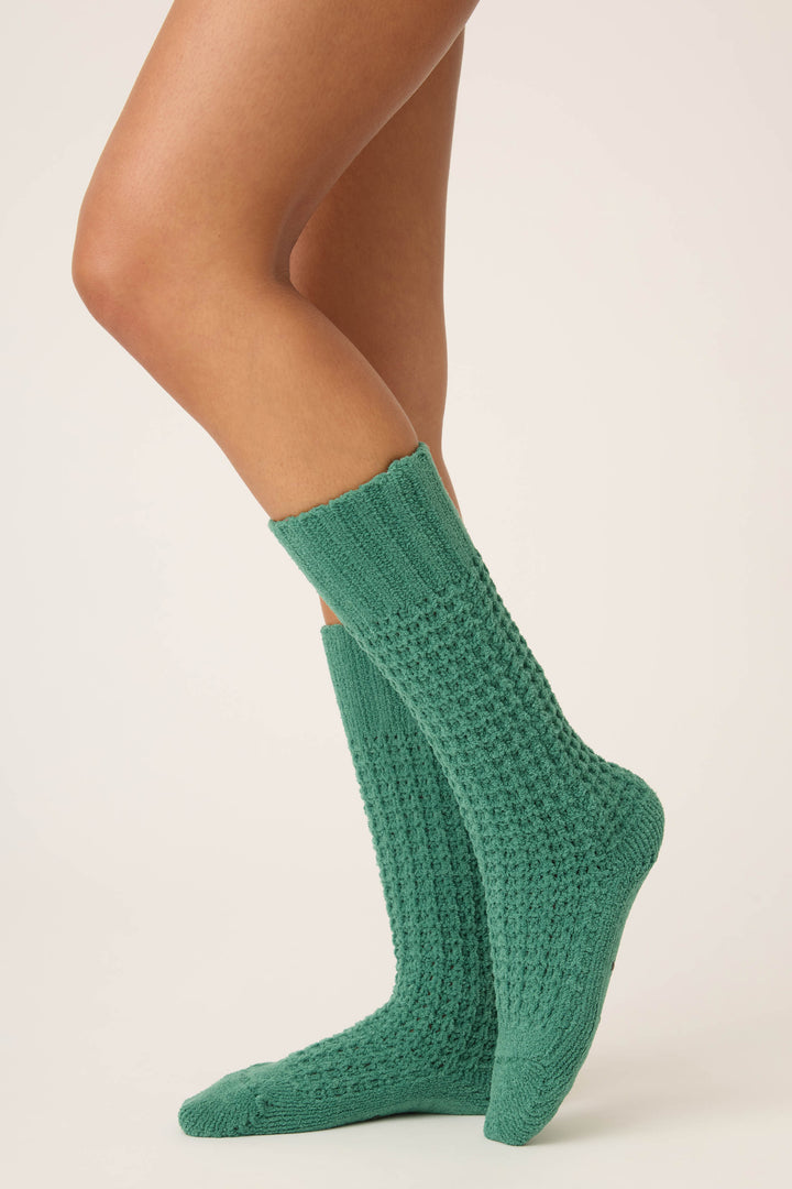 A person models P.J. Salvage Chenille Waffle Solid Crew Socks in green, balancing on one foot with the other knee bent, against a plain light background. Only their legs and feet are shown.
