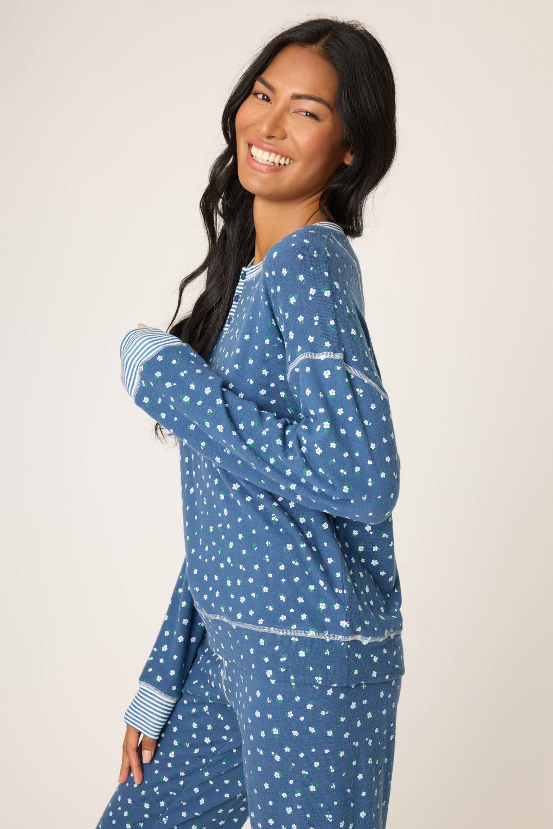 A person with long dark hair smiles and winks at the camera while wearing the P.J. Salvage Cozy Life Floral Long Sleeve Top, standing against a plain light background.