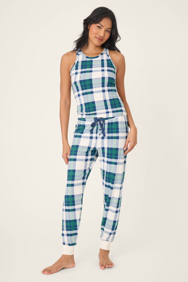 A woman stands barefoot against a plain light background, wearing P.J. Salvage's Cozy Life Plaid Velour Thermal Banded Pant in blue, green, and white plaid with a matching sleeveless top.