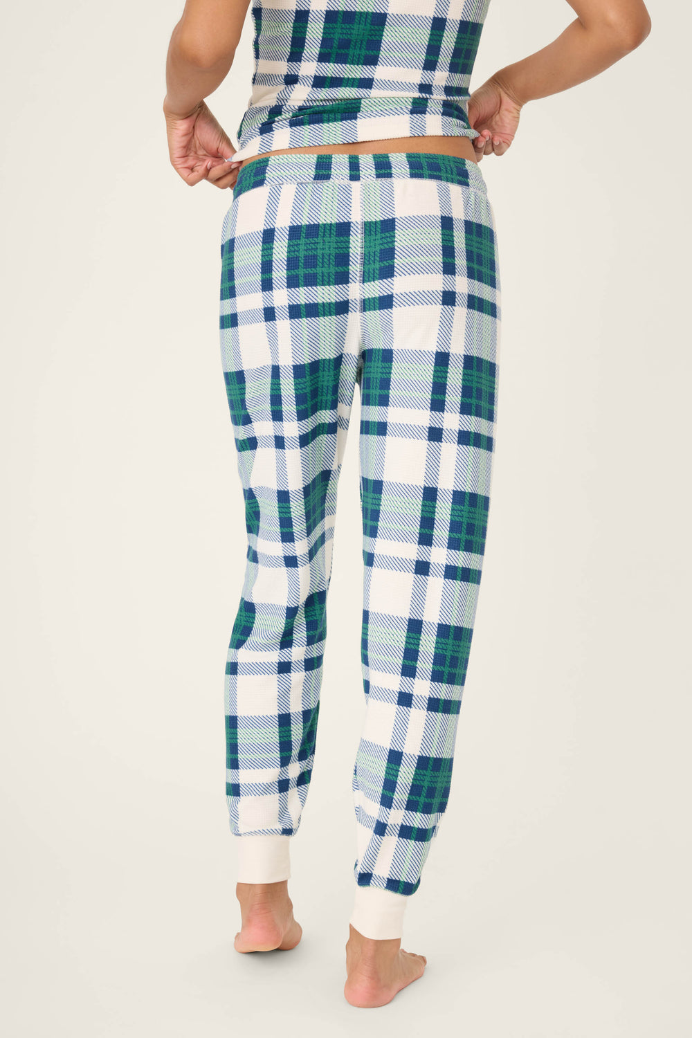 A person is shown from the back wearing P.J. Salvage's Cozy Life Plaid Velour Thermal Banded Pant in blue, green, and white plaid with a matching top, barefoot on a plain light background.
