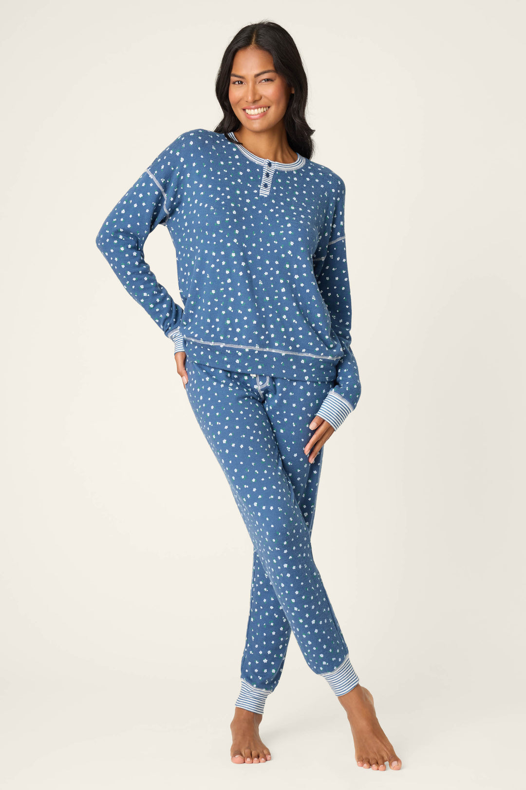 A person stands barefoot against a light background, smiling with one hand on their hip while wearing the Cozy Life Floral PJ Set by P.J. Salvage.