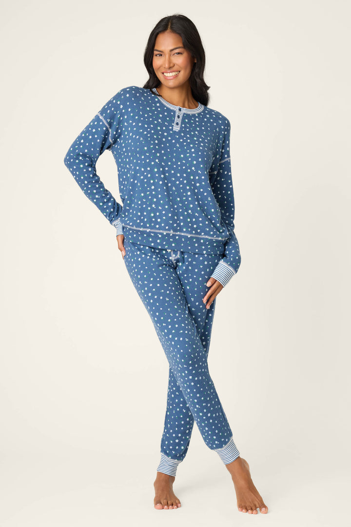A person stands barefoot against a light background, smiling with one hand on their hip while wearing the Cozy Life Floral PJ Set by P.J. Salvage.
