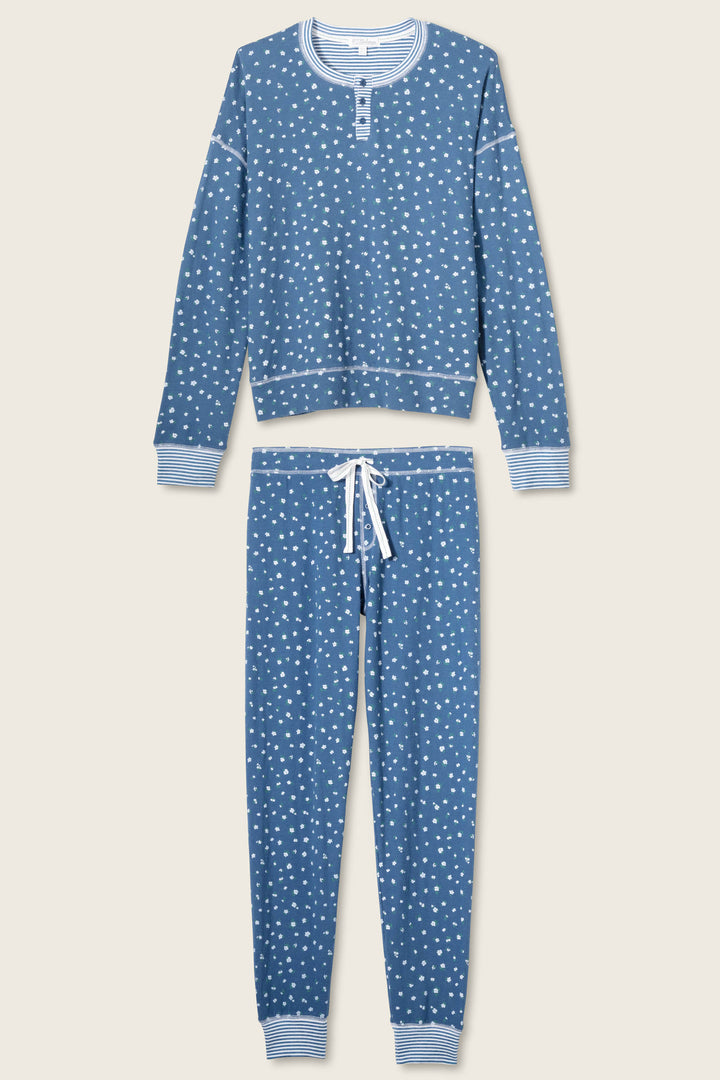 The P.J. Salvage Cozy Life Floral PJ Set features a blue background with white polka dots, a long-sleeve top with white trim and buttons, plus drawstring pants with a white waist tie and striped cuffs.