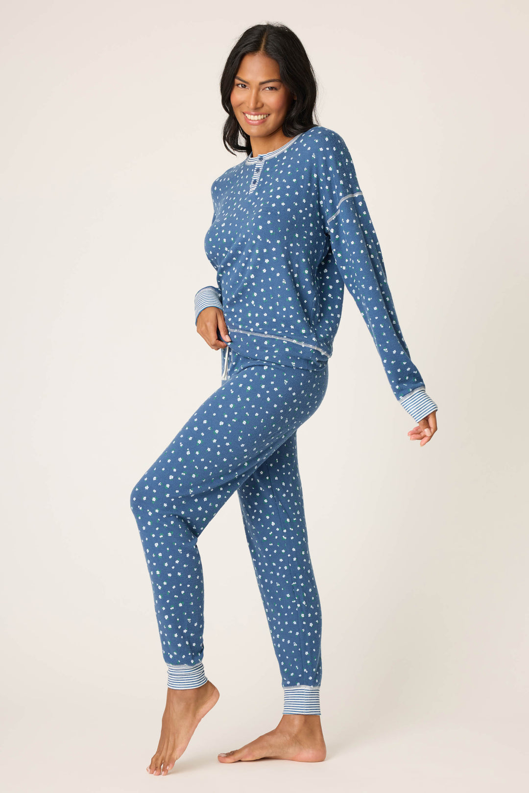 A woman stands barefoot against a plain background, smiling and lifting one foot slightly, wearing the P.J. Salvage Cozy Life Floral PJ Set.
