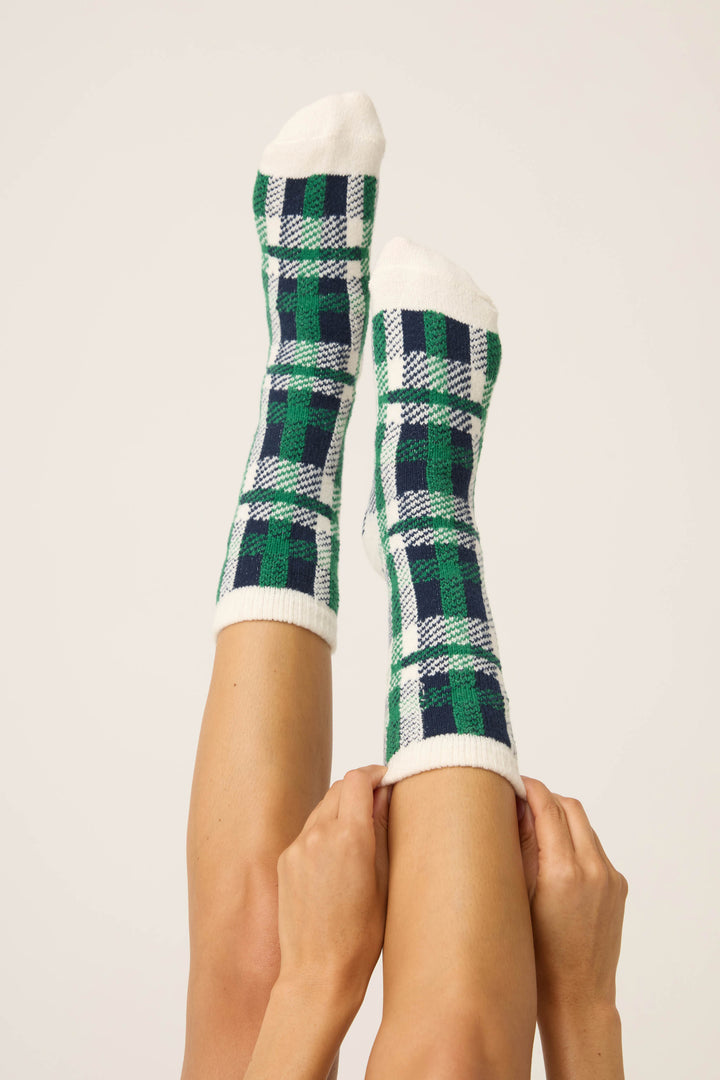 A pair of legs raised in the air, hands holding ankles, model Cozy Life Plaid Crew Socks by P.J. Salvage in green, blue, white, and black against a plain light background.