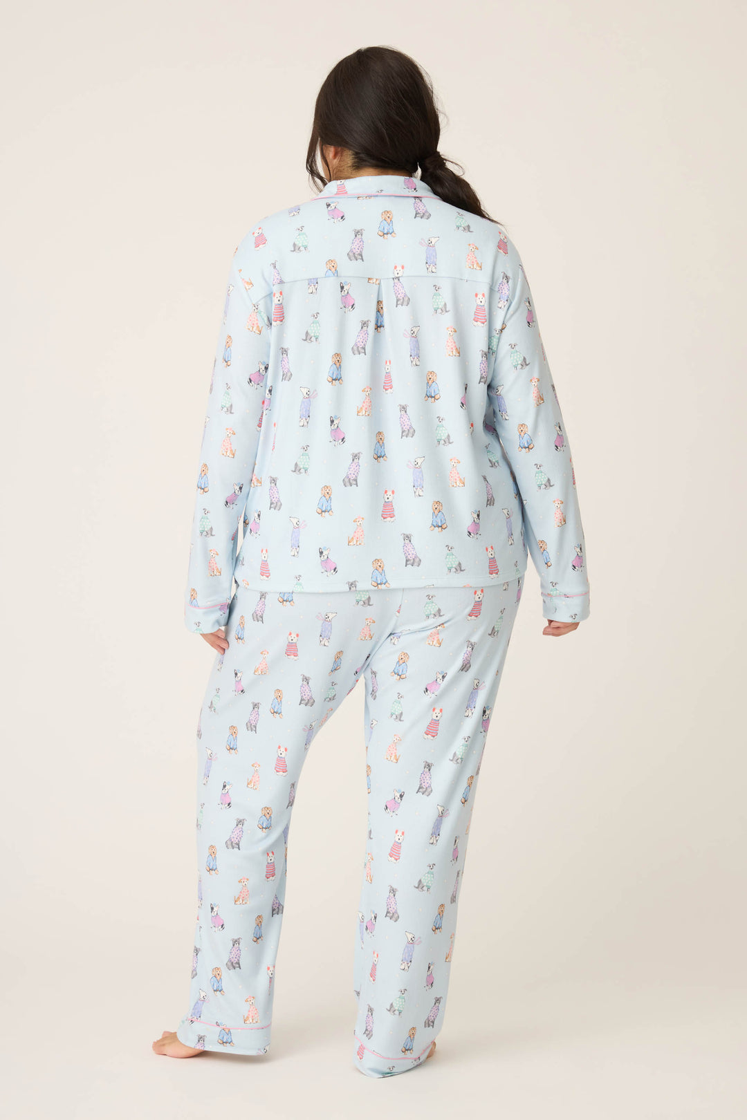 A person with long dark hair models the P.J. Salvage Doggone Cold Dog Print Pointelle Plus Size PJ Set, standing barefoot and facing away from the camera against a plain background.