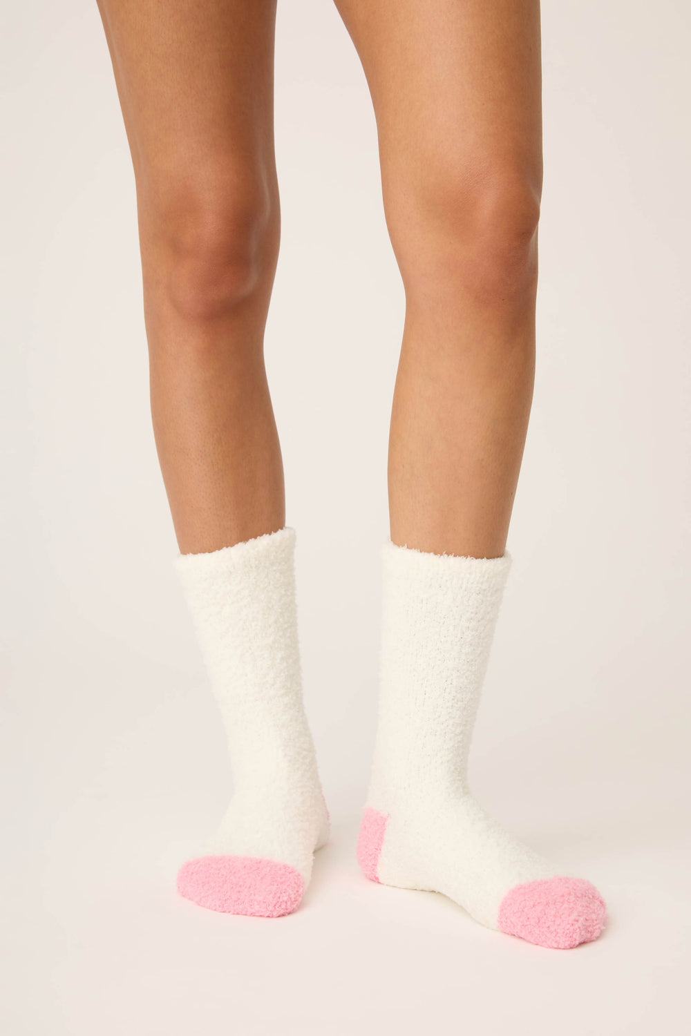 A person wears P.J. Salvage Doggone Cold Fuzzy Dog Crew Socks—white with pink toes and heels—standing on a light-colored surface, with only their lower legs and feet visible.