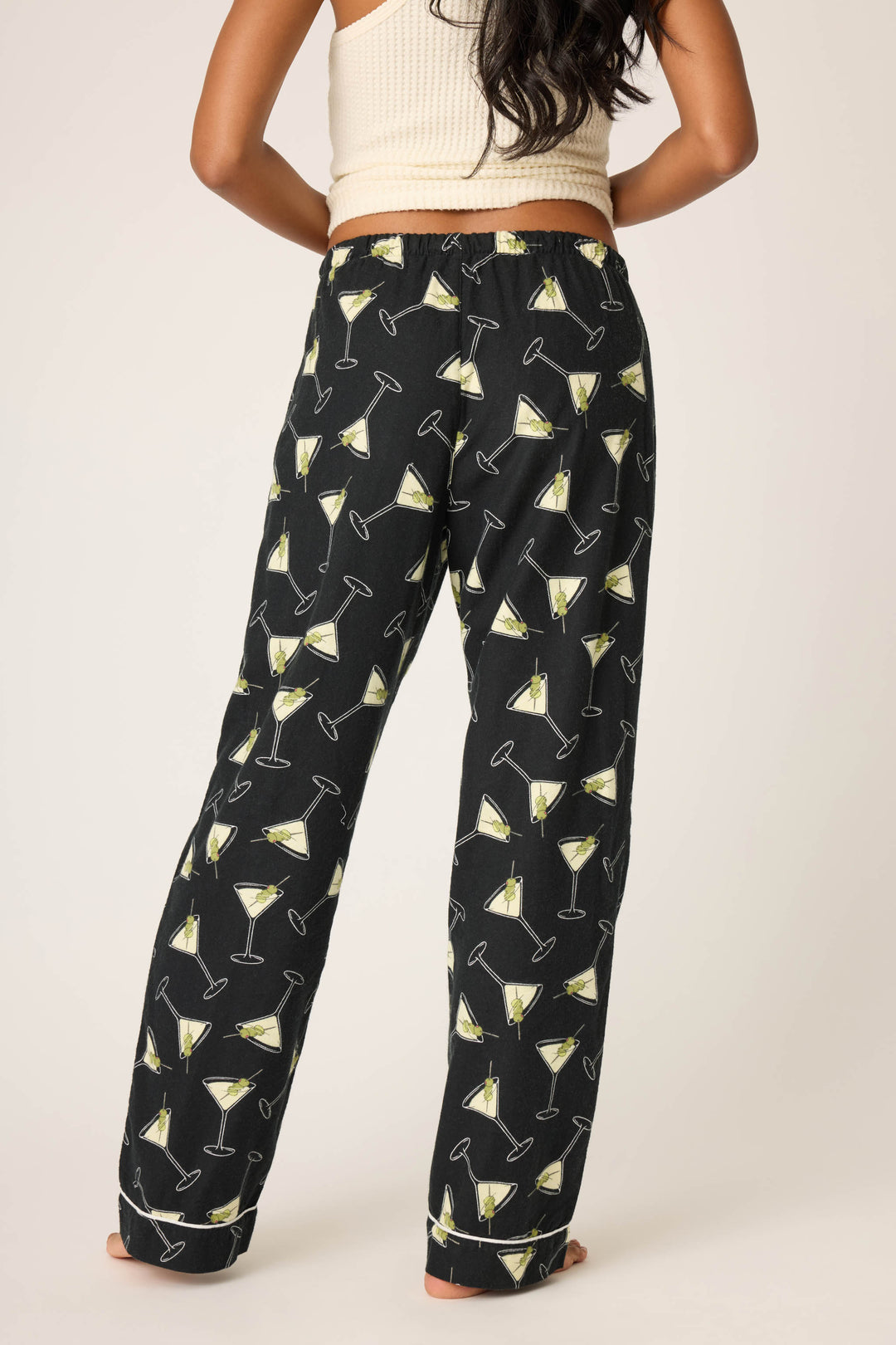 A person stands barefoot, facing away from the camera, wearing P.J. Salvage Merrier With A Martini Flannel Pants with a martini glass pattern and a beige sleeveless top against a plain light background.
