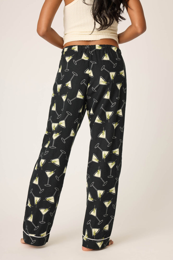 A person stands barefoot, facing away from the camera, wearing P.J. Salvage Merrier With A Martini Flannel Pants with a martini glass pattern and a beige sleeveless top against a plain light background.