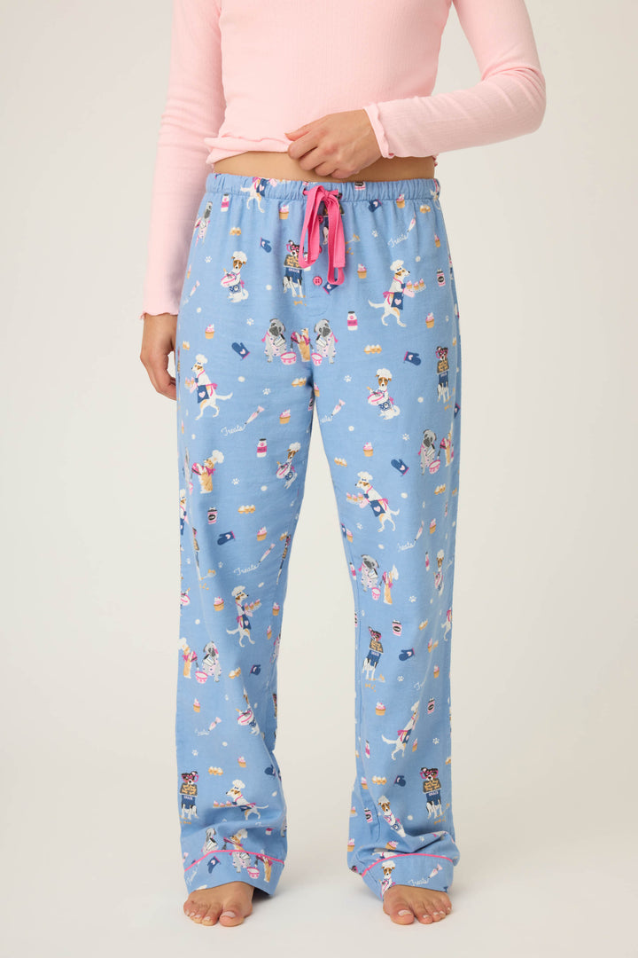 A person models P.J. Salvages WILD PANT FLANNELS—light blue pajama pants with a cartoon dog print and pink drawstring—paired with a long-sleeved pink top, standing barefoot against a plain background.