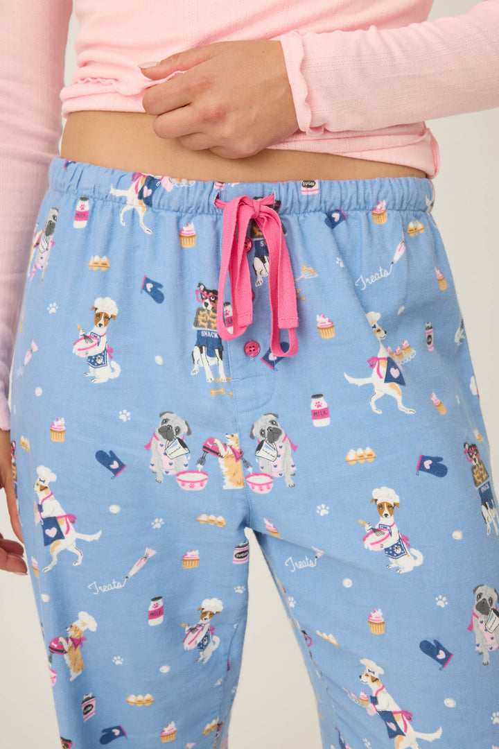 A person wearing P.J. Salvage WILD PANT FLANNELS in light blue with a pink drawstring and a dog, cupcake, bone, and Treats print, paired with a light pink long-sleeve shirt.