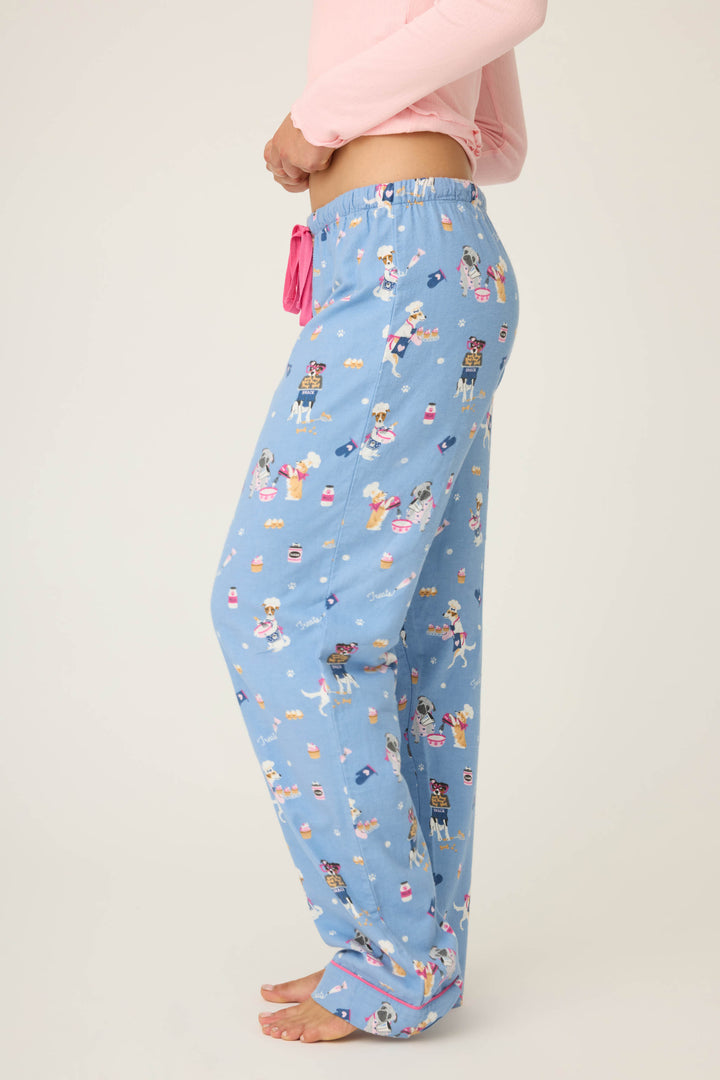 A person stands barefoot in P.J. Salvage WILD PANT FLANNELS—light blue pajama pants with playful dog print and a pink drawstring—paired with a light pink long-sleeve top, shown in side view against a plain background.