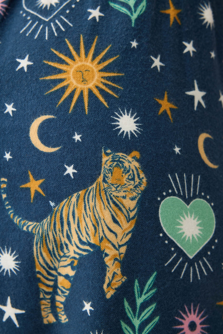 A close-up of WILD PANT FLANNELS by P.J. Salvage, showing tigers, yellow stars, crescent moons, sunbursts, green hearts with white starbursts inside, and leafy shapes on a dark blue background.