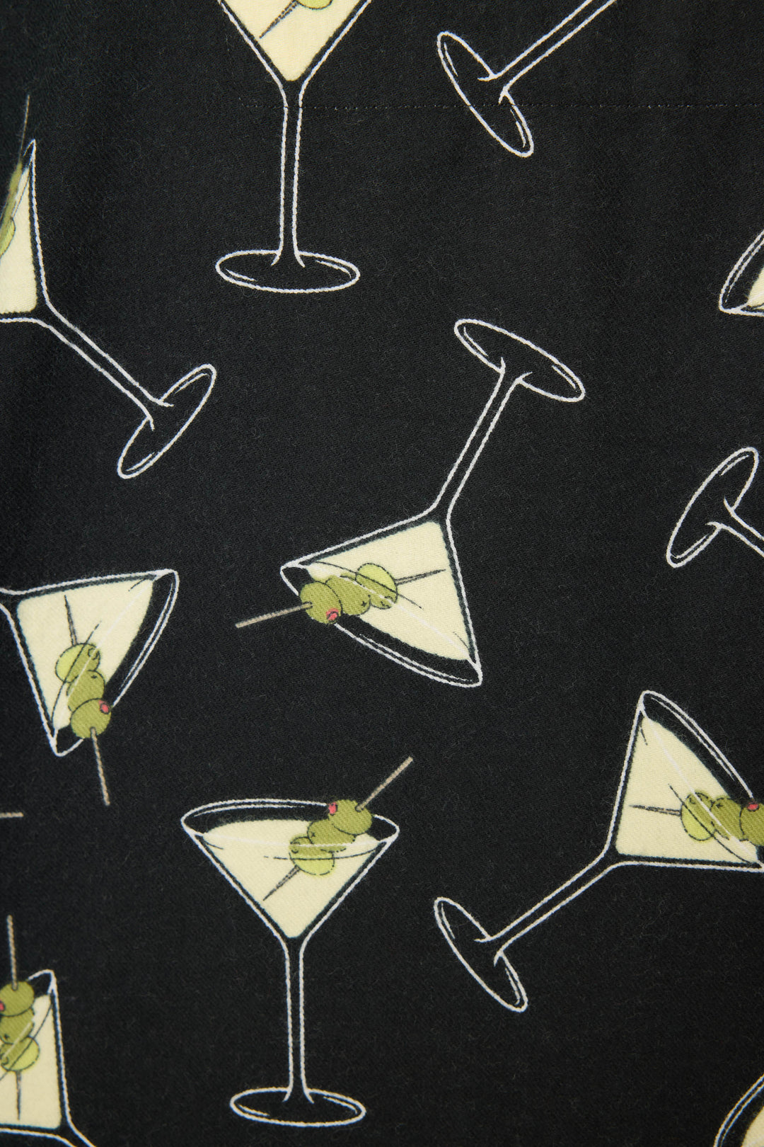 The Merrier With A Martini Flannel PJ Set by P.J. Salvage features black fabric adorned with martini glasses filled with yellow liquid and green olive garnishes, arranged at various angles.