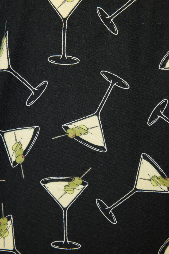The Merrier With A Martini Flannel PJ Set by P.J. Salvage features black fabric adorned with martini glasses filled with yellow liquid and green olive garnishes, arranged at various angles.