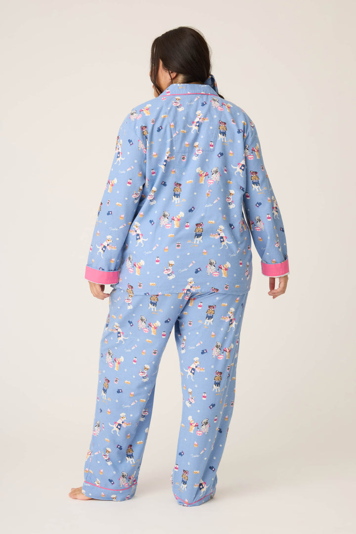 A person with long dark hair is seen from behind, barefoot, wearing the P.J. Salvage 3-Piece Set WILD PJ SET FLANNELS PLUS—blue pajamas with a playful print and pink cuffs—against a plain light background.