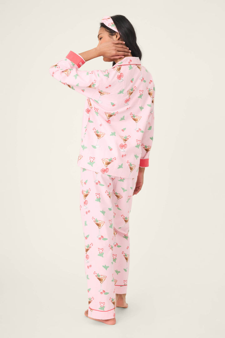 A person stands facing away in the P.J. Salvage Tini Time Drink Print Flannel PJ Set, featuring pink cuffs and a matching headband. One hand touches their neck against a plain light background.