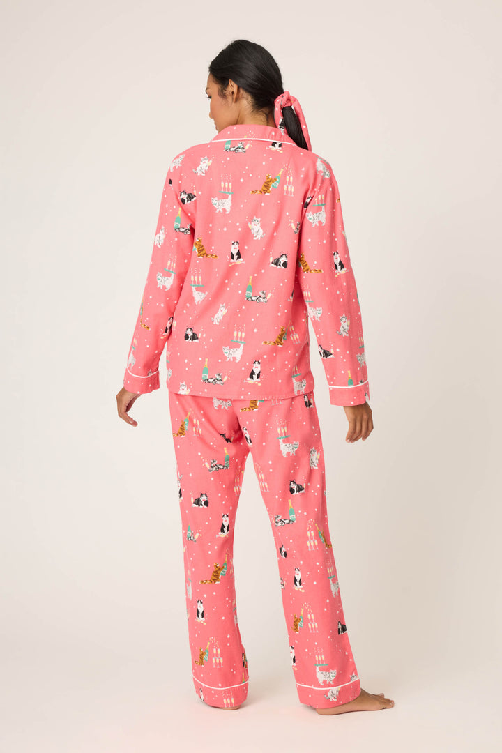 A person stands barefoot facing away, wearing the Let’s Get Fizzical Cat Print Flannel PJ Set by P.J. Salvage. Their dark hair is tied back with a pink ribbon, set against a plain, light background.
