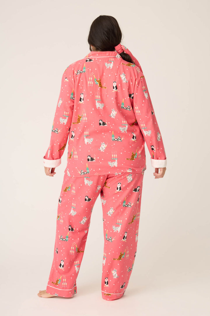 A person faces away from the camera in P.J. Salvage's Let's Get Fizzical Cat Print Flannel Plus Size PJ Set, featuring matching pink long-sleeve top and loose pants with a cat print and white cuffs, against a plain light background.