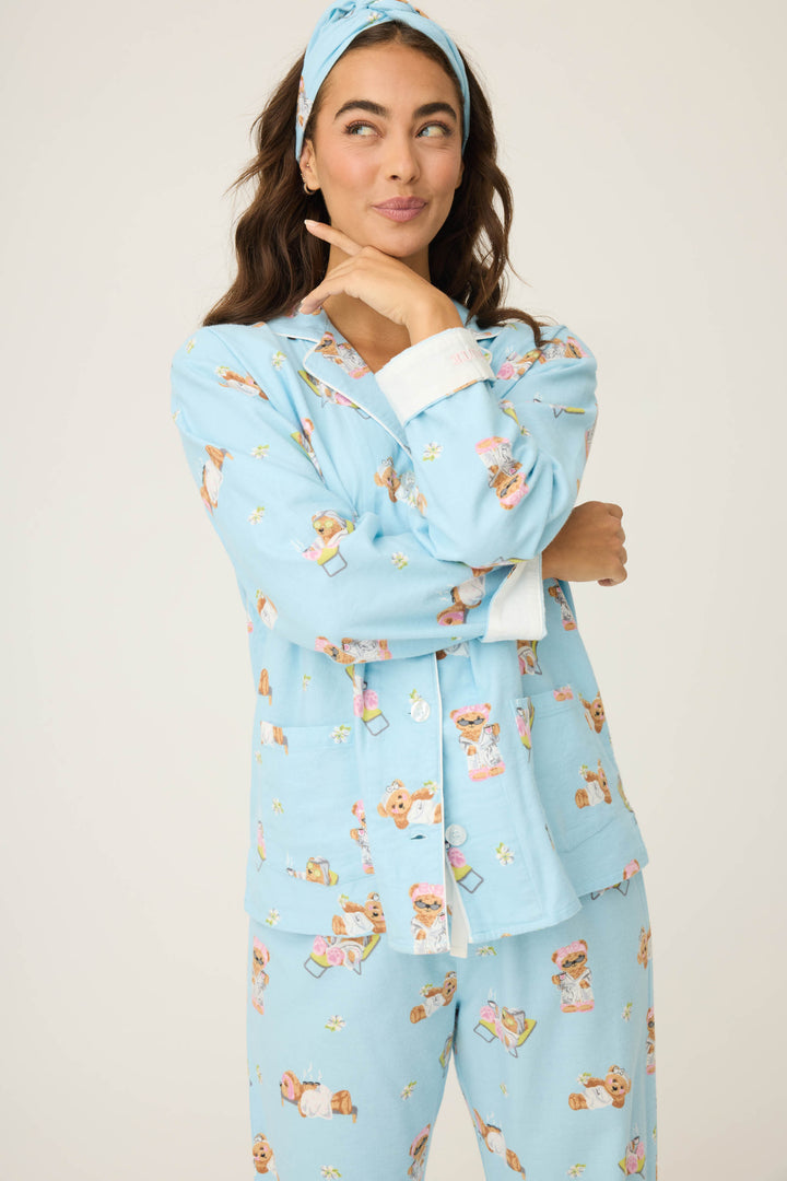 A person with long brown hair, wearing a blue P.J. Salvage Beary Cute Bear Print Flannel PJ Set, stands with one arm crossed and the other hand touching their chin, looking to the side.