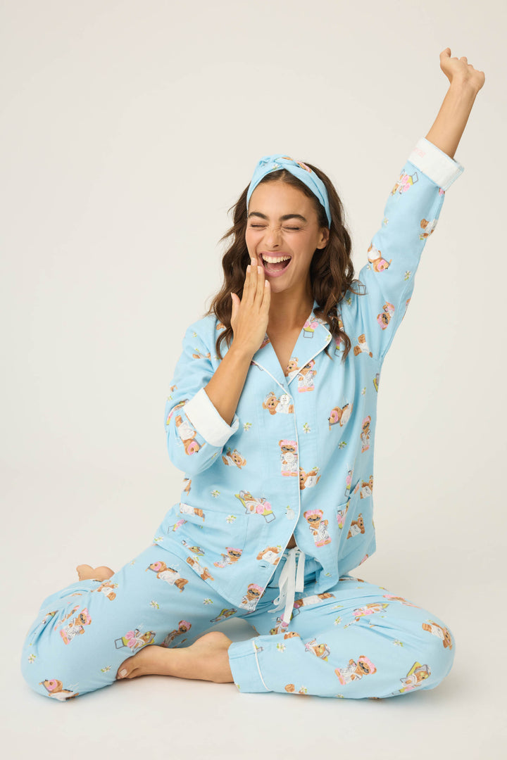 Wearing the P.J. Salvage Beary Cute Bear Print Flannel PJ Set and a headband, a person sits cross-legged on the floor, stretching one arm up and covering their mouth as if yawning.