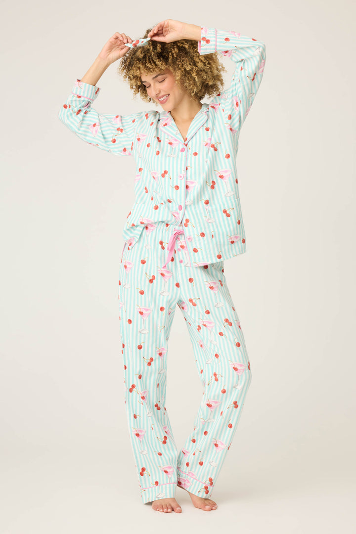 A person smiles barefoot in P.J. Salvages 3-Piece Set PAISLEY PJ SET FLANNELS, featuring light blue and white stripes with a pink and red cherry print, standing against a plain light background with hands raised overhead.