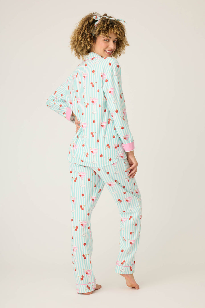 A woman stands barefoot, facing away and smiling at the camera, wearing the P.J. Salvage 3-Piece Set PAISLEY PJ SET FLANNELS with matching striped pajamas, pink flamingos, pink cuffs, and a coordinating hair scrunchie against a white background.