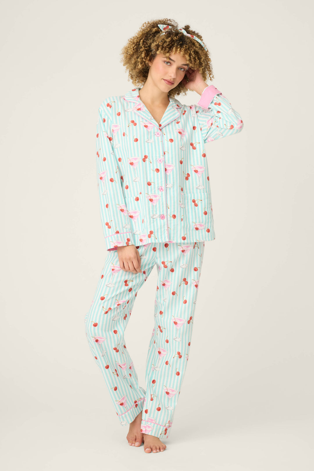 A person with curly hair and a matching hair accessory wears the P.J. Salvage 3-Piece Set PAISLEY PJ SET FLANNELS—matching long-sleeve striped pajamas with pink flamingo and heart patterns plus pink cuffs.