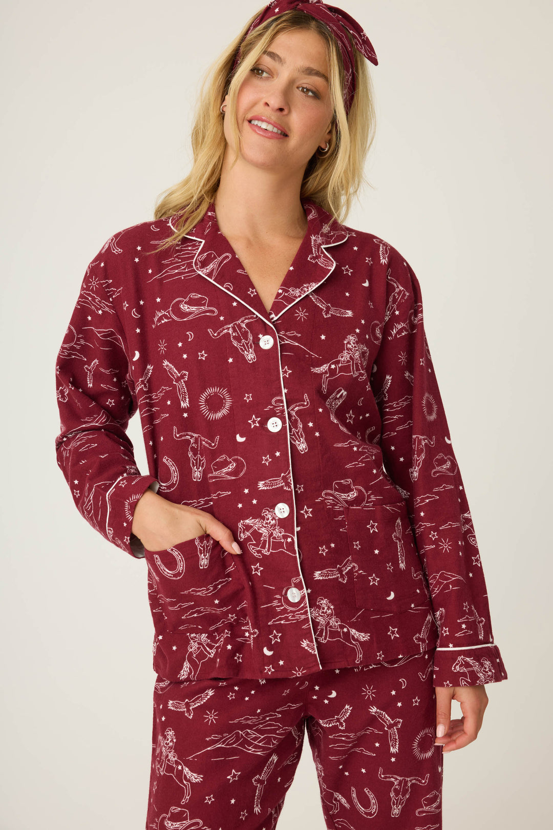 A person with long blonde hair wears the P.J. Salvage 3-Piece Set Paisley PJ Set Flannels—maroon pajamas with white constellation and celestial prints, plus a matching headband, standing with one hand in their pocket.