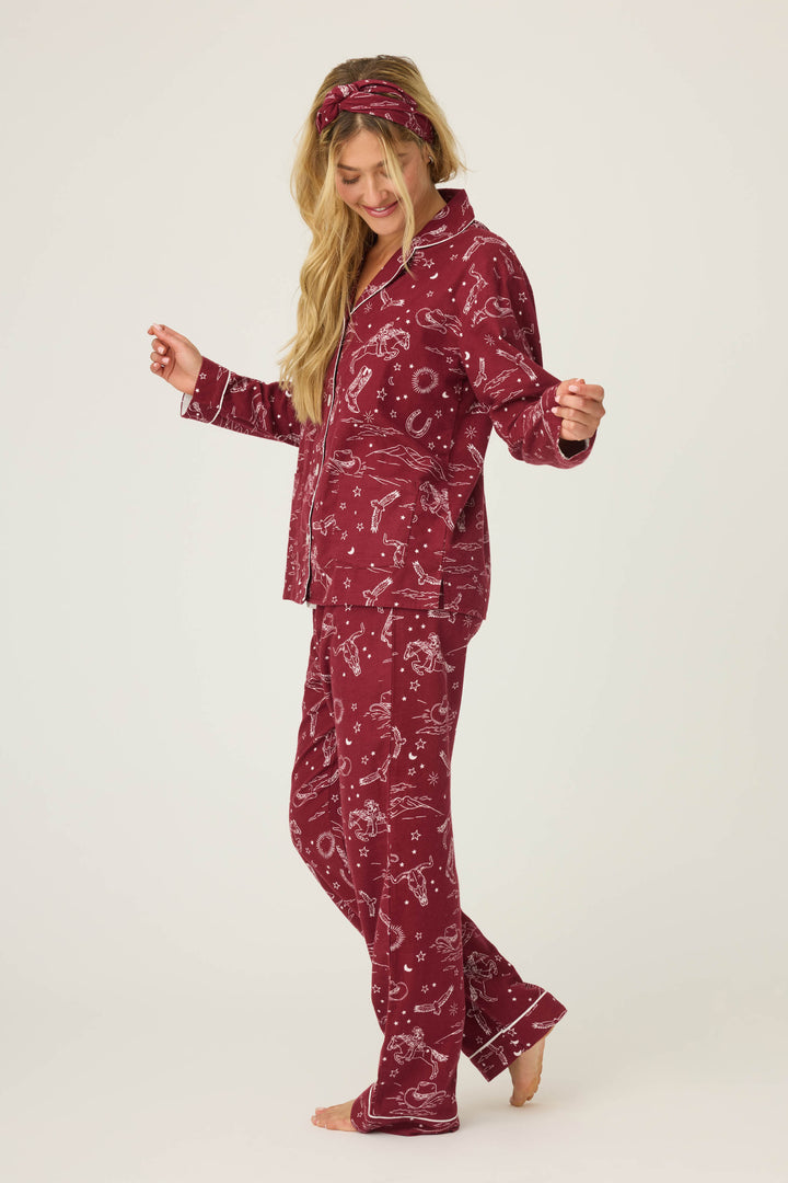 A woman with long blonde hair smiles while looking down, wearing the P.J. Salvage 3-Piece Set PAISLEY PJ SET FLANNELS: a matching maroon pajama set with white print and headband. She stands barefoot against a plain, light background.