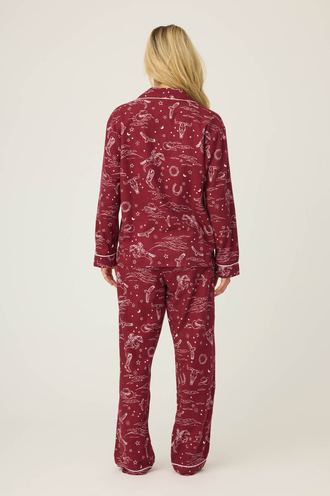 A person with long blonde hair faces away, wearing the P.J. Salvage 3-Piece Set PAISLEY PJ SET FLANNELS featuring a matching burgundy top and pants with white paisley prints. The background is plain and light-colored.