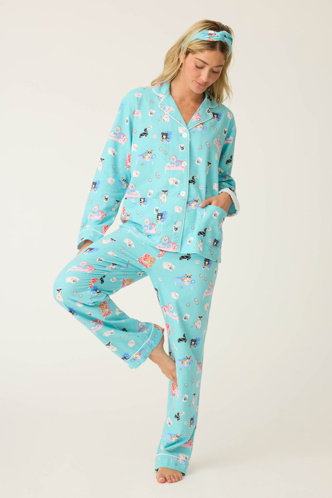 A model in the P.J. Salvage This Is How I Roll Dog Print Flannel PJ Set stands on one leg, hand in pocket, wearing a matching headband and looking downward against a plain white background.