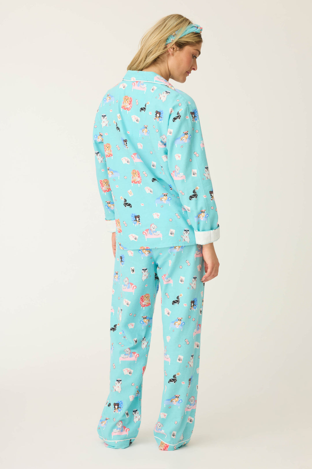 A person stands with their back to the camera, wearing P.J. Salvages This Is How I Roll Dog Print Flannel PJ Set—light blue pajamas with a playful dog print and a matching headband—set against a plain background.