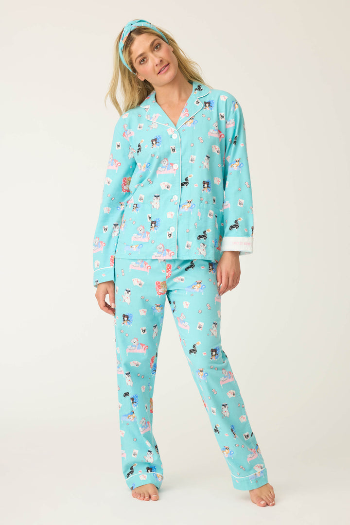 A woman stands barefoot against a plain background in the P.J. Salvage This Is How I Roll Dog Print Flannel PJ Set—light blue, relaxed fit with a collared, button-up top—paired with a matching whimsical headband.