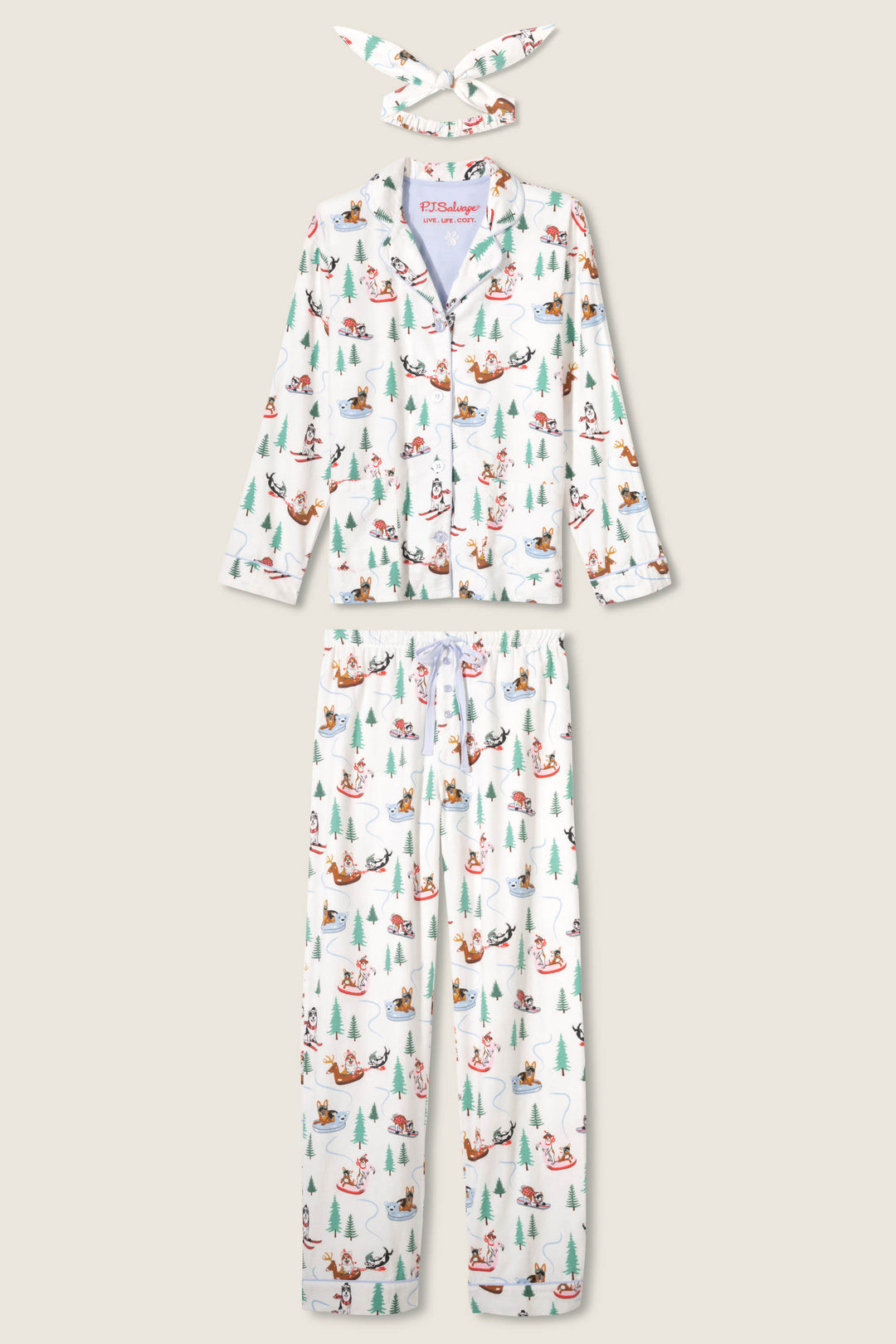 The P.J. Salvage Sleigh All Day Winter Print Flannel PJ Set includes a white button-up top, matching pants, and headband with a colorful holiday dog and tree print, shown on a plain light background.